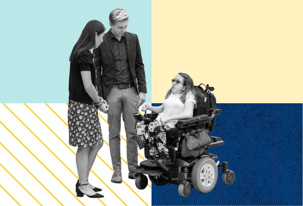 Two people standing and talking to another person who is using a wheelchair