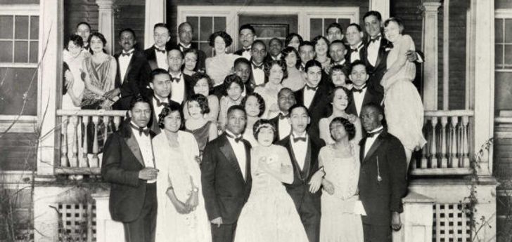 A vintage photo of Black students in formal wear posing together on a porch