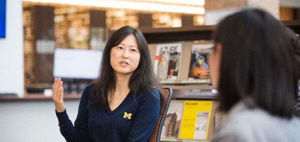 A woman wearing a U-M sweater having a conversation in a library